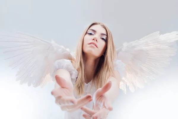 Een engel uit de hemel geeft u een hand. Jonge, prachtige blonde meisje in de afbeelding van een engel met witte vleugels. — Stockfoto