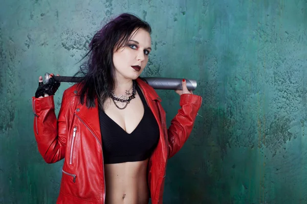 Punk woman with a bat in red leather jacket, standing against the wall — Stock Photo, Image