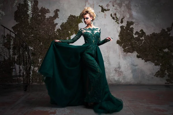 Retrato de mujer rubia atractiva joven en un hermoso vestido verde. Fondo texturizado, interior. Peinado de lujo —  Fotos de Stock