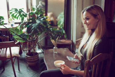 Genç kadın serbest meslek sahibi vintage kafede kanepede otururken cep telefonunda sohbet