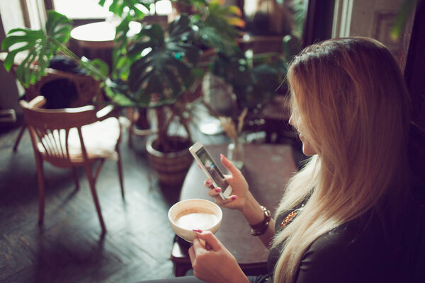 Молодая женщина фрилансер болтает по мобильному телефону, сидя на диване в винтажном кафе
