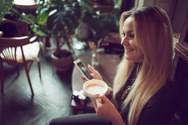 Молода фрілансерка спілкується на мобільному телефоні, сидячи на дивані в старовинному кафе — стокове фото