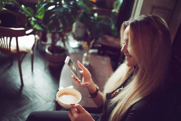Молода фрілансерка спілкується на мобільному телефоні, сидячи на дивані в старовинному кафе — стокове фото
