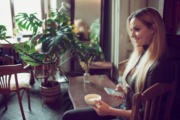 Unga kvinnliga freelancer chattar på mobiltelefon medan du sitter i soffan i vintage café — Stockfoto