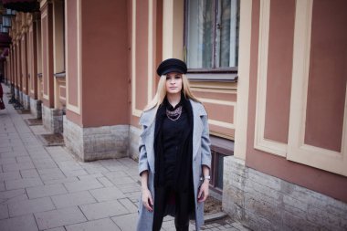 Genç, kalça ve çekici sarışın kız şık bir şapka ve gri bir ceket şehirde yürüyüş