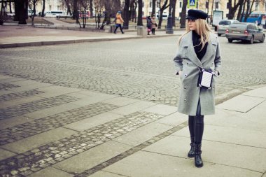 Genç, kalça ve çekici sarışın kız şık bir şapka ve gri bir ceket şehirde yürüyüş