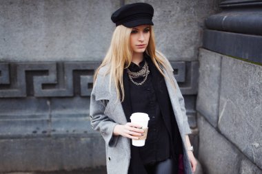 Gitmek için kız şık bir şapka ve gri bir ceket kahve ile şehir dolaşan genç, kalça ve çekici sarışın