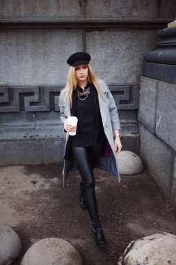 Gitmek için kız şık bir şapka ve gri bir ceket kahve ile şehir dolaşan genç, kalça ve çekici sarışın