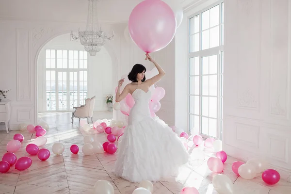 Jovem em vestido de noiva em interior de luxo com uma massa de balões rosa e branco . — Fotografia de Stock