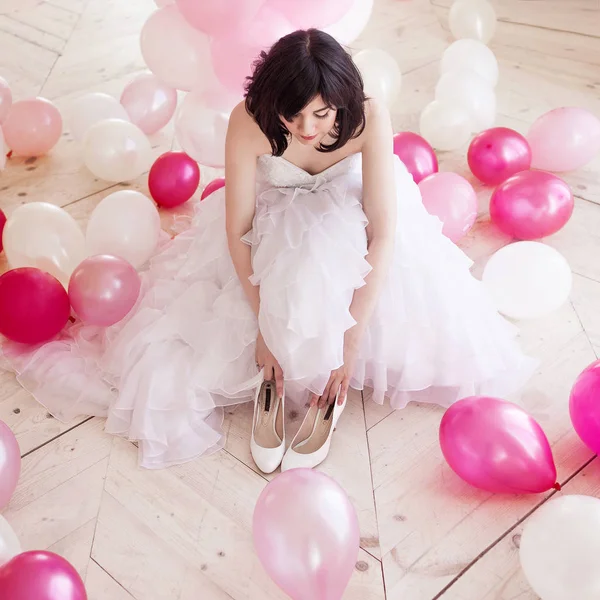 Młoda kobieta w sukni ślubnej w luksusowe wnętrze o masie różowe i białe balony. Trzymać w ręce jej białe buty — Zdjęcie stockowe