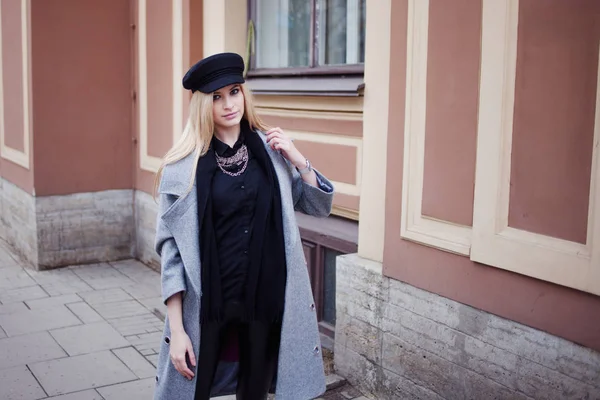 Joven, cadera y atractiva rubia paseando por la ciudad, chica con un sombrero elegante y un abrigo gris — Foto de Stock