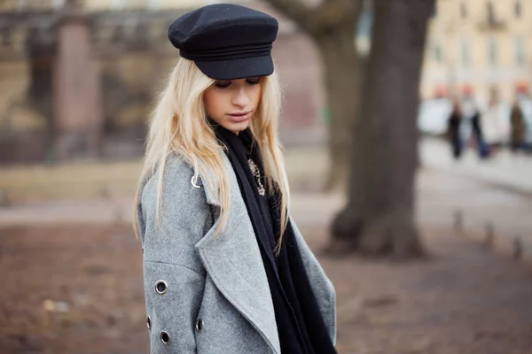 若い、ヒップで魅力的な金髪の少女のスタイリッシュな帽子は、グレーのコート、街を歩く — ストック写真