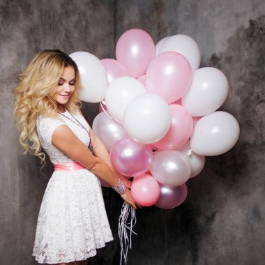 Partide balonlar büyük bir demet tutan büyüleyici genç sarışın ile pembe kanat, beyaz elbiseli.