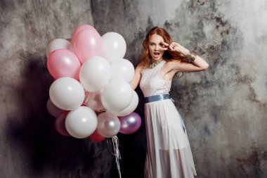 Partide balonlar büyük bir demet tutan Kızıl saçlı güzellik genç kadın beyaz bir elbise içinde.