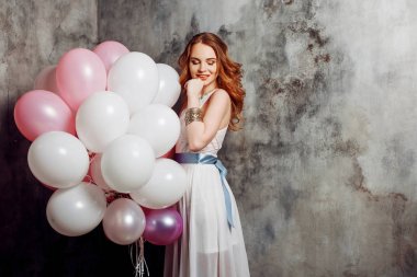 Partide balonlar büyük bir demet tutan Kızıl saçlı güzellik genç kadın beyaz bir elbise içinde.