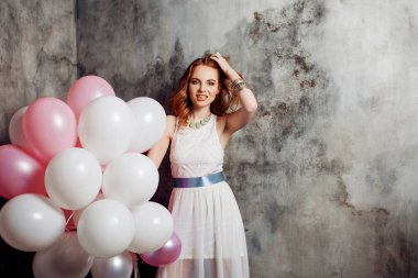 Partide balonlar büyük bir demet tutan Kızıl saçlı güzellik genç kadın beyaz bir elbise içinde.