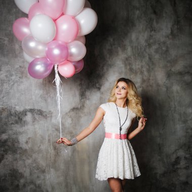 Partide balonlar büyük bir demet tutan büyüleyici genç sarışın ile pembe kanat, beyaz elbiseli.