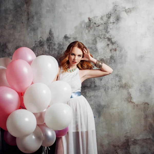Partide balonlar büyük bir demet tutan Kızıl saçlı güzellik genç kadın beyaz bir elbise içinde.