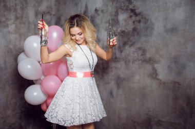 Pembe kanat ile beyaz elbiseli çekici genç sarışın iki şişe soda elleri mutlu ve neşeli balon kızla dans. Gri dokulu arka plan üzerinde