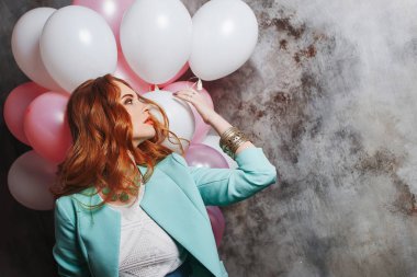 Balonlar büyük bir demet partide tutan Kızıl saçlı güzellik genç kadın beyaz bir elbise içinde. Balonlar ile mutlu ve neşeli kız. Gri dokulu arka plan üzerinde