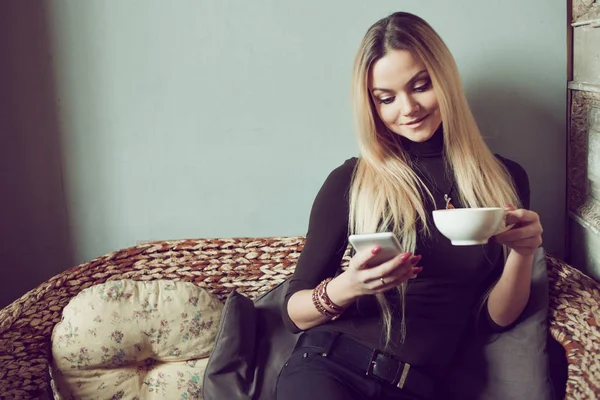 Young female freelancer chatting on mobile phone while sitting on the couch in vintage cafe — Stock Photo, Image