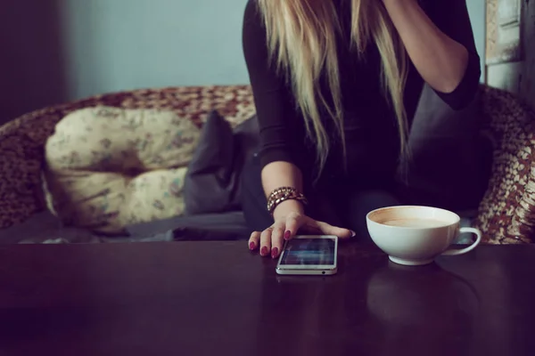 Young charming female freelancer chatting on mobile phone while sitting on the couch in vintage cafe. Drink morning coffee and reading text message during work in comfortable coffee shop — Stock Photo, Image