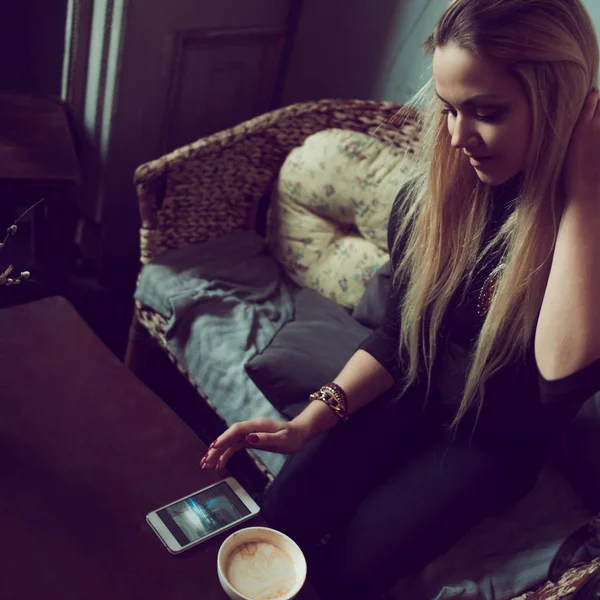 Mladí okouzlující ženské freelancer chatování na mobilním telefonu, zatímco sedí na gauči v retro kavárně. Vypít ranní kávu a číst textové zprávy při práci v příjemné kavárně — Stock fotografie