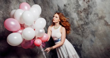 Büyük balon demeti partide tutan Kızıl saçlı güzellik genç kadın beyaz elbiseli. Gri dokulu arka plan üzerinde