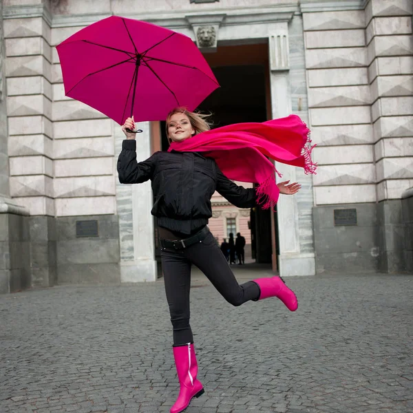 Belle jeune et heureuse femme blonde avec parapluie coloré dans la rue. Fille dans une écharpe rose vif, bottes en caoutchouc et parapluie marche dans une ville pluvieuse . — Photo