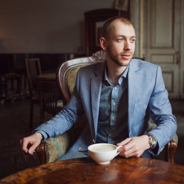 Genç adam oturur ve kahve sabah sahiptir. Portre iç