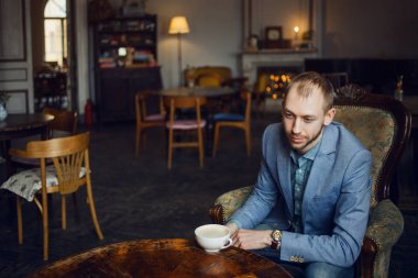 Genç adam oturur ve kahve sabah sahiptir. Portre iç