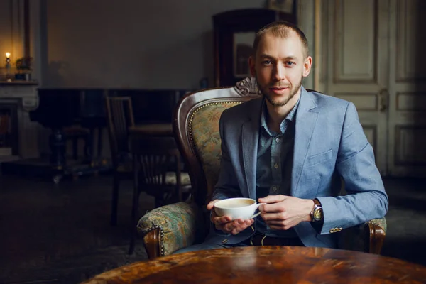 Mladý muž sedí a těší se na kávu ráno. Portrét v interiéru — Stock fotografie