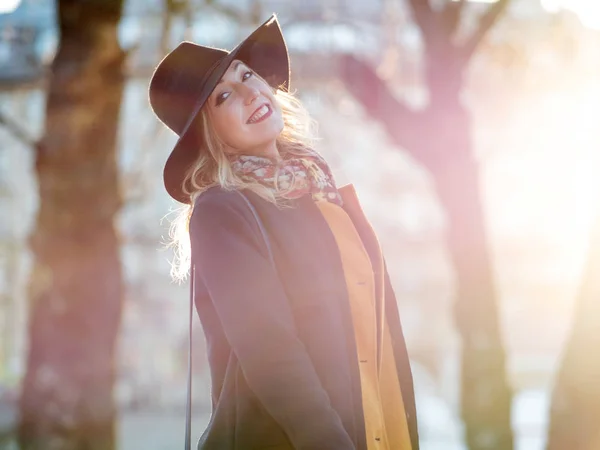 Mujer joven divertida en sombrero elegante y bufanda, caminando. Retrato de la encantadora rubia de la calle. Luz solar brillante y sombreado en tonos cálidos — Foto de Stock