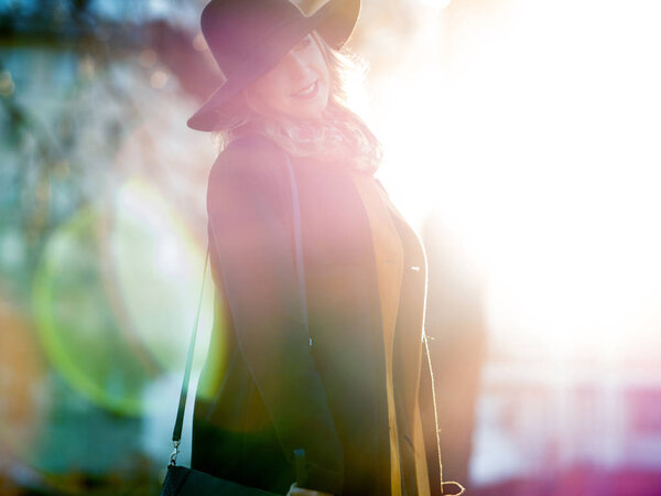 Funny young woman in elegant hat and scarf, walking. Portrait of the charming blonde on the street. Bright sunlight and shading in warm tones