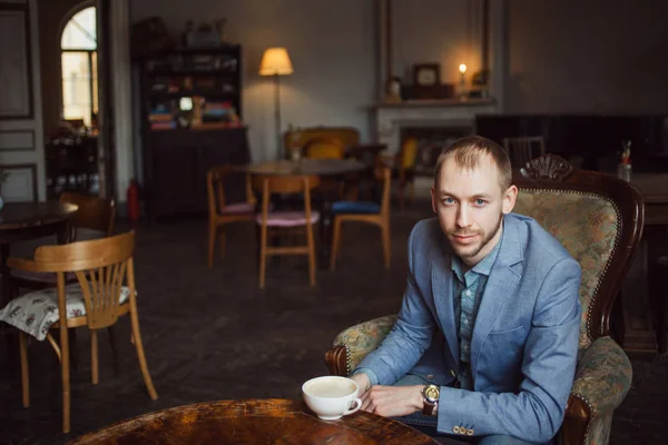 Young man sits and enjoys coffee in the morning. Portrait in the interior — Stock Photo, Image