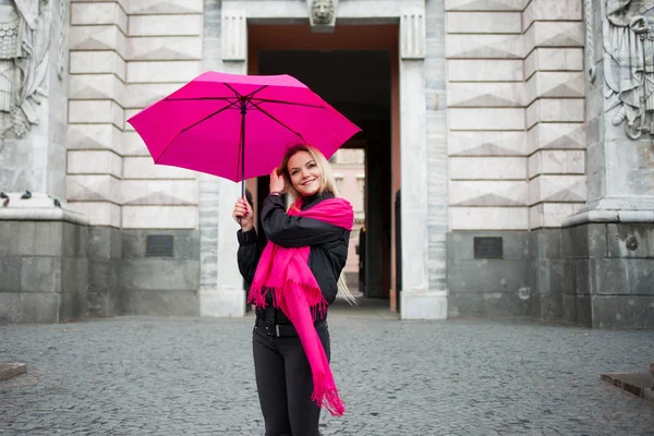 Молодая и счастливая женщина с разноцветными пуговицами на улице. Понятие позитивности и оптимизма. Девушка в ярко-розовом шарфе и зонтике гуляет по дождливому городу . — стоковое фото