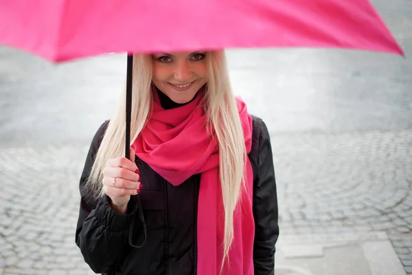 Sad pensive girl standing under a bright umbrella on the street. The concept of positivity and optimism. Girl in a bright pink scarf and umbrella walking in a rainy city. — Stock Photo, Image