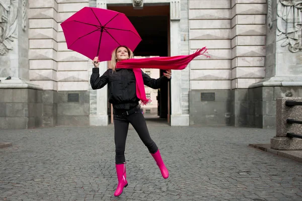 Piękna młoda i szczęśliwy kobieta blond z kolorowym parasolem na ulicy. Koncepcja optymizm i pozytywne nastawienie. Dziewczynka jasny różowy szalik, kalosze i parasol — Zdjęcie stockowe