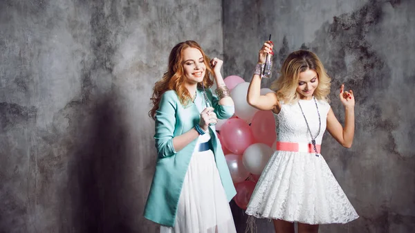 Blonde en roodharige. Twee jonge charmante vriendinnen op het feest met ballonnen. Op grijze gestructureerde achtergrond — Stockfoto