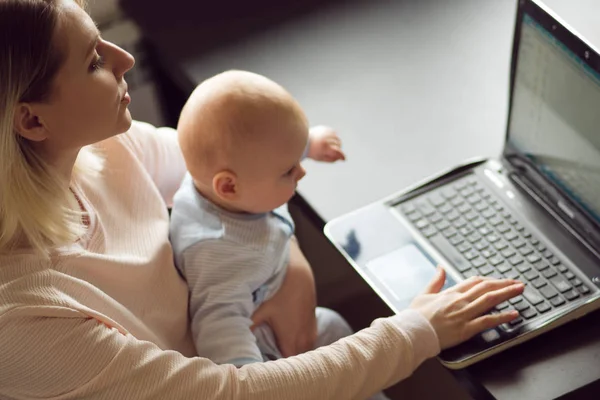 Jovem mãe em casa escritório com computador e seu bebê. Freelancer ou blogueiro, trabalho e cuidados infantis . — Fotografia de Stock