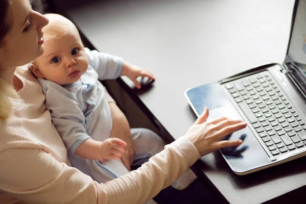 Νέοι όμορφη ξανθιά γυναίκα, τη μητέρα στο γραφείο στο σπίτι με τον υπολογιστή και το μωρό. Εργασία και παιδικής φροντίδας. — Φωτογραφία Αρχείου