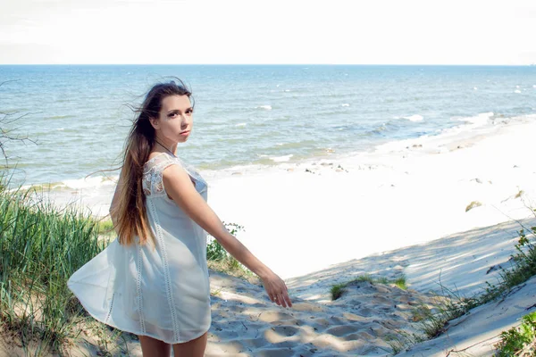 Giovane donna bruna affascinante sulla costa del mare. Bella ragazza in un breve abito estivo bianco — Foto Stock