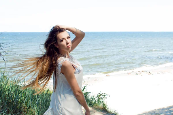 Jovem mulher morena encantadora na costa do mar. Menina bonita em um vestido de verão branco curto — Fotografia de Stock