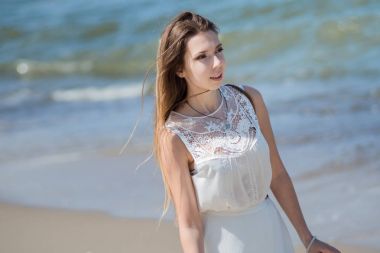 Deniz kıyısında genç sevimli esmer kadın. Beyaz yazlık elbise güzel kız. Dalgalar deniz arka plan üzerinde