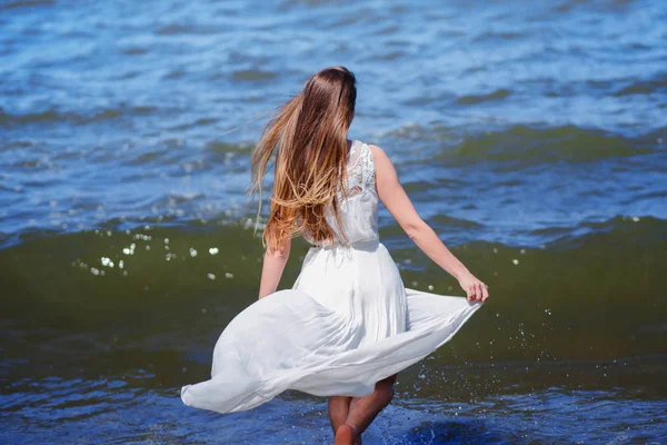 Jonge charmante brunette vrouw op Zeekust. Mooi meisje in een witte zomerjurk. Loopt naar de zee, terug weergave — Stockfoto