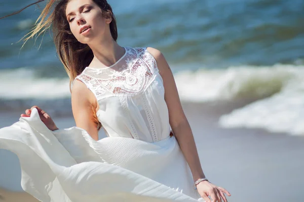 Young charming brunette woman on sea coast. Beautiful girl in a white summer dress. Runs towards the sea — Stock Photo, Image
