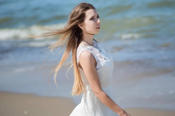 Ung charmig brunett kvinna vid havet. Vacker flicka i en vit sommarklänning. På bakgrund av havets vågor — Stockfoto