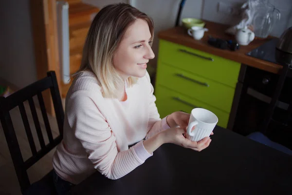 Ung blond kvinna hemma. Flickan håller kopp te, stående i köket — Stockfoto