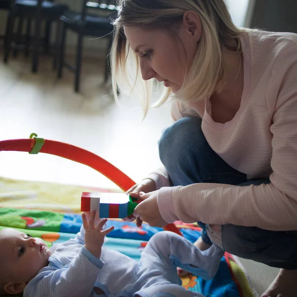 Joven madre y niño jugando juntos en el interior, en el suelo. Mamá le da a hijo un juguete —  Fotos de Stock