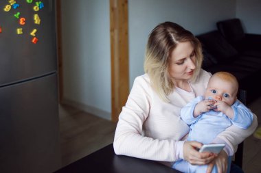 Genç anne bebekle oturur ve telefon kullanır. Internet tarama, kapalı